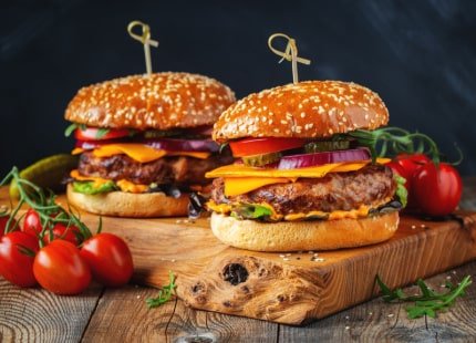 Two burgers of beef, cheese and vegetables on an old wooden table